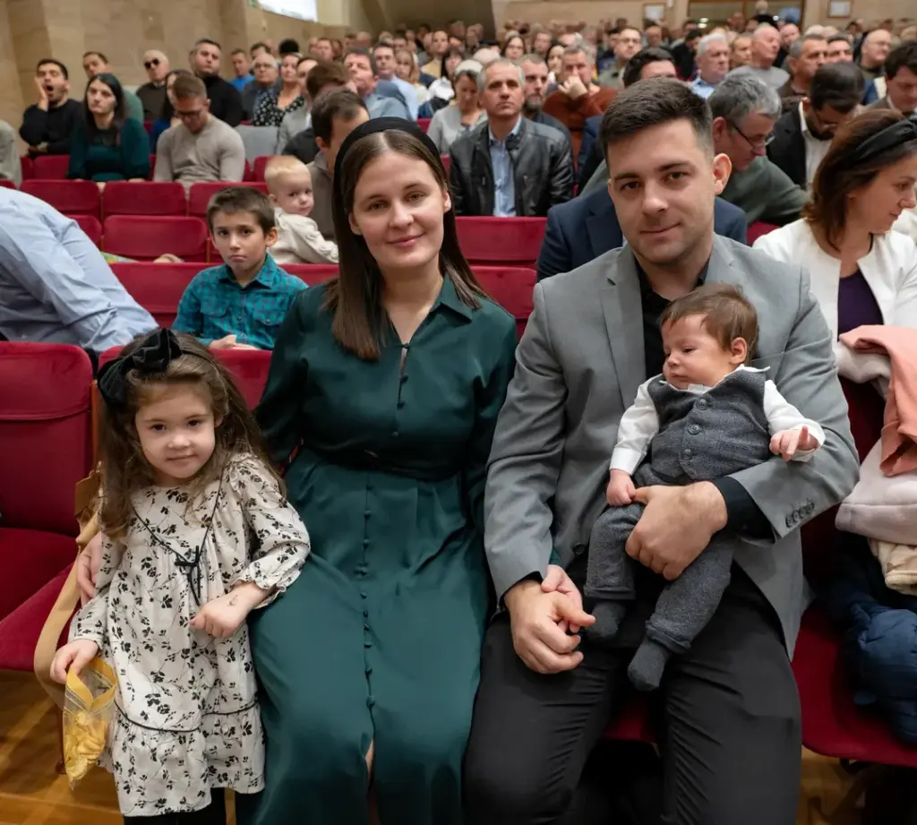 O familie tânără cu copiii, zâmbind, în sala Bisericii Elim
